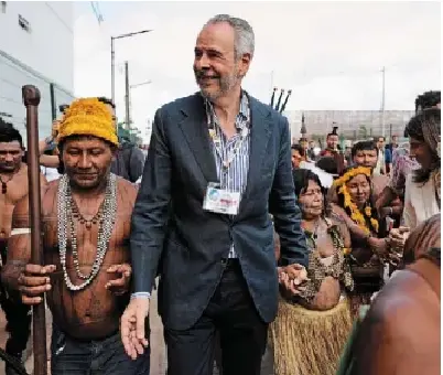 André Corrêa do Lago, COP30 pres­id­ent, holds the hand of an Indi­gen­ous woman as he walks with a group out­side the venue for the COP30 UN Cli­mate Sum­mit on Frida in Belém, Brazil.