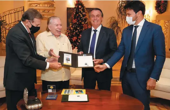 Em ca­sa. Bol­so­na­ro exi­be se­lo alu­si­vo aos 90 anos de Silvio San­tos, na re­si­dên­cia do apre­sen­ta­dor em SP; ao la­do, Flo­ri­a­no Pei­xo­to Ne­to (E) e Fa­bio Fa­ria (D)