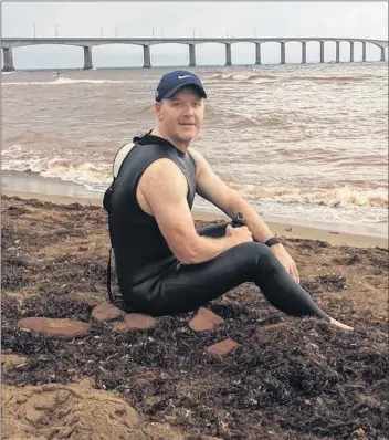 Ryan Bradley, shown sit­ting on the shore near the Con­fed­er­a­tion Bridge, will at­tempt to swim the Northum­ber­land Strait on Sun­day.