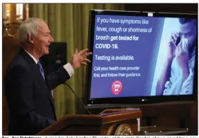 Gov. Asa Hutchin­son, dur­ing his daily brief­ing Thurs­day at the state Capi­tol, shows an ad for a new cam­paign aimed at get­ting more peo­ple tested for the coro­n­avirus.