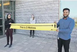 Pub­lic-health in­spec­tors hold a two-me­tre long sign to en­cour­age phys­i­cal dis­tanc­ing in Kingston Wed­nes­day.