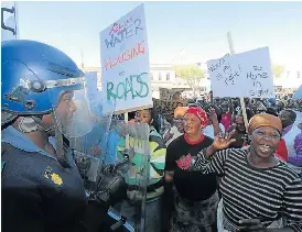Bear­ing the brunt: An­gry Makhanda res­i­dents con­front riot po­lice out­side the city hall, call­ing for the prov­ince to step in and run the Makana Mu­nic­i­pal­ity. On Thurs­day a court or­dered the dis­so­lu­tion of the mu­nic­i­pal­ity.