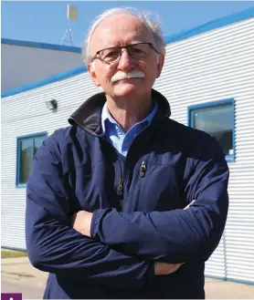 Tom Nes­mith, membre de l’as­so­cia­tion ma­ni­to­baine des ar­chives et an­cien pro­fes­seur d’ar­chives au Dé­par­te­ment d’his­toire de l’uni­ver­si­té du Ma­ni­to­ba. Der­rière, le bâ­ti­ment ac­tuel des ar­chives de la Ville.